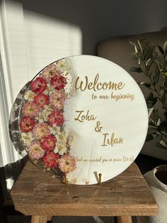 a welcome plate with flowers on it sitting on a table next to a potted plant