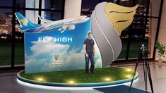 a man standing in front of an advertisement for a flight high airliner on display