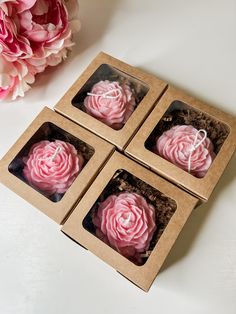 three pink cupcakes sitting in a box on a table next to some flowers