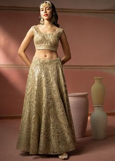 This lehenga set features heavy gold zari embroidery with mirrorwork. The short sleeves blouse has a plunging neckline. The lehenga set shows delicate tassels details. It is paired with a mirror embroidered organza dupatta with tassels on both sides. Gold Pre-draped Saree With Intricate Embroidery For Reception, Floor-length Sharara With Gold Embroidery For Diwali, Gold Embroidered Palazzo Set For Festivals, Gold Lehenga With Mirror Work For Eid, Gold Floor-length Pre-draped Saree With Resham Embroidery, Festive Gold Lehenga With Mirror Work, Bollywood Style Gold Palazzo Set With Embroidery, Gold Floor-length Palazzo Set With Zari Work, Gold Dola Silk Sets With Mirror Work