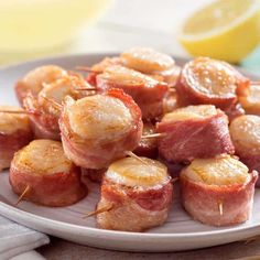 a white plate topped with bacon wrapped in toothpicks next to lemon wedges