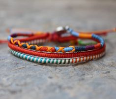 two colorful bracelets sitting on top of a stone floor next to an orange string