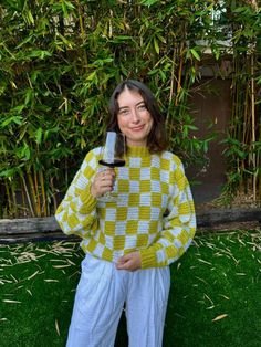 a woman holding a wine glass in front of her face while wearing a yellow and white checkered sweater