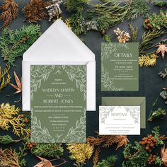 the wedding stationery is surrounded by evergreen leaves and pine cones, which are accented with greenery