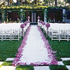 an outdoor ceremony with white chairs and purple flowers on the aisle leading up to it