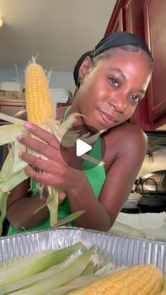 a woman holding corn in her hands while standing next to a tin pan filled with it