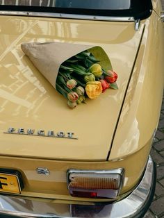 an old yellow car with tulips and other flowers on it's hood