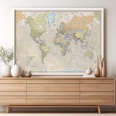 a large world map hangs on the wall above a dresser with vases and plants