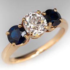 three stone engagement ring in yellow gold with an oval diamond center and blue sapphire side stones