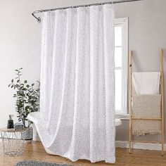 a white shower curtain in a bathroom next to a chair and rug on the floor