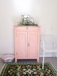 a pink cabinet sitting next to a white chair and potted plant on top of it