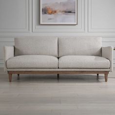 a white couch sitting on top of a hard wood floor next to a framed painting