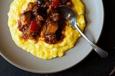 a white plate topped with grits covered in meat and veggies next to a fork