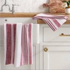 a kitchen sink with two towels hanging from the faucet and a wooden cutting board