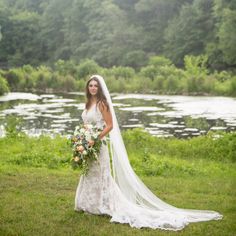 a woman in a wedding dress holding a bouquet and standing next to a river with trees