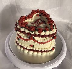 a heart shaped cake with red roses on the bottom and white frosting is sitting on a plate