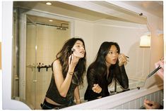 two women are brushing their teeth in front of the mirror and one is looking at her reflection