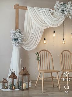 two wooden chairs sitting next to each other in front of a white drape covered wall