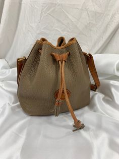 "Measurements are 10\" wide, 10\" high, 5\"7 deep and a 33\" adjustable shoulder strap and a 13\" drop. One main compartment, unlined with a top drawstring closure. Bag has brass hardware with tan leather trim, hang tag and bag is exactly as pictured. There are a few light scuffs and light marks on corners with no tears, one minor ink stains bottom and the shoulder strap is adjustable. Bag is 100% genuine Dooney & Bourke made in USA with serial#A2 696571. I WANT TO STRESS THAT THIS ITEM IS VINTA Vintage Brown Tote Bucket Bag, Vintage Everyday Bucket Bag With Removable Pouch, Vintage Bucket Bag With Removable Pouch For Everyday, Vintage Tote Bucket Bag For Travel, Vintage Beige Bucket Bag, Vintage Travel Tote Bucket Bag, Vintage Travel Bucket Tote Bag, Vintage Crossbody Bucket Bag, Vintage Bucket Bag With Adjustable Strap