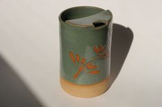 a green vase sitting on top of a white table next to a shadow from the wall