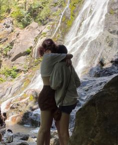 two people hugging each other in front of a waterfall