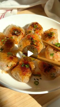 a white plate topped with dumplings and chopsticks on top of a wooden table