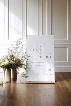 a white sign sitting on top of a wooden floor next to two vases filled with flowers