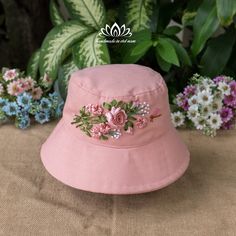 a pink hat with flowers on it sitting in front of some green leaves and flowers