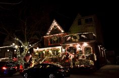 a house covered in christmas lights with cars parked on the street next to it at night