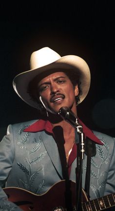 a man in a cowboy hat singing into a microphone while holding a guitar and wearing a blue suit