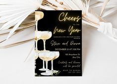 a black and white wedding card with champagne glasses on it, next to palm leaves