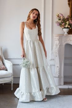 a woman in a white dress standing next to a chair and holding a flower bouquet