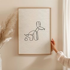 a person is holding up a drawing in front of a wall with a plant next to it