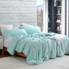 a bed with blue comforters and pillows in a room next to a brick wall