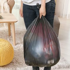 a woman is holding a plastic bag in her hands while standing next to a couch