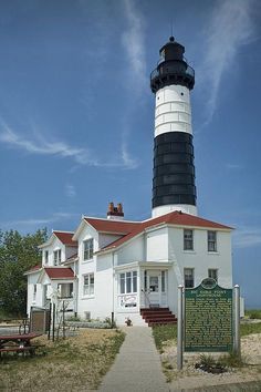 a white and black light house with a red roof next to a sign that says the lighthouse