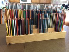 there are many different colored pencils in the wooden holder on the counter top,