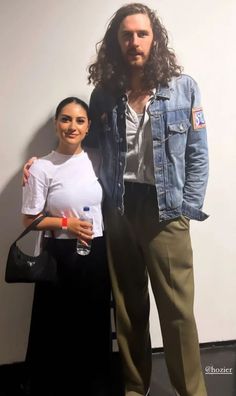 a man and woman standing next to each other in front of a wall with a painting on it