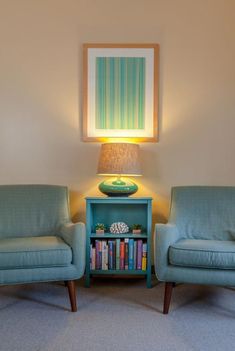 two blue chairs sitting next to each other in front of a table with a lamp on it