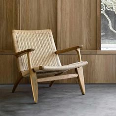 a wooden chair sitting in front of a window next to a wall with wood paneling