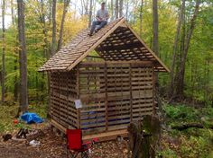 a man sitting on top of a wooden structure in the woods