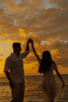 a man and woman dancing on the beach at sunset