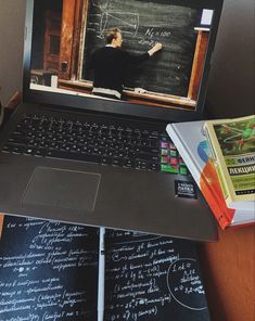 an open laptop computer sitting on top of a desk next to notebooks and books