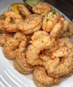 some fried food on a white plate next to a lemon wedge and a pickle