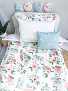 a bed with floral sheets and pillows on top of it next to a potted plant