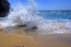 an ocean wave hitting on the beach with rocks