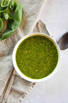 a white bowl filled with green pesto next to two spoons and a napkin