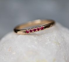 a yellow gold ring with three red stones on top of it, sitting on a rock