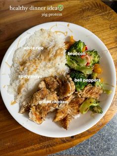 a white plate topped with meat, rice and broccoli on top of a wooden table