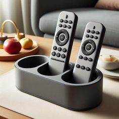 two remote controls are sitting in a cup holder on a table next to a plate with fruit